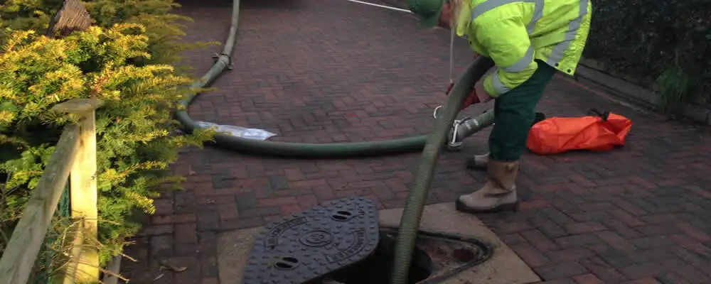 Septic tank cleaning technician servicing a septic tank with a vacuum hose in Modesto, CA