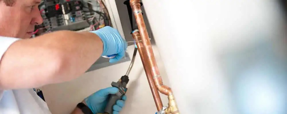 Water heater repair technician testing copper pipe connections and controls in Modesto, CA